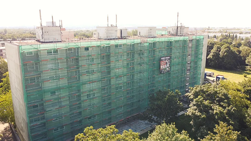 Langgestreckter Wohnblock in Düsseldorf, vollflächig mit Gerüst und Schutznetz eingehaust