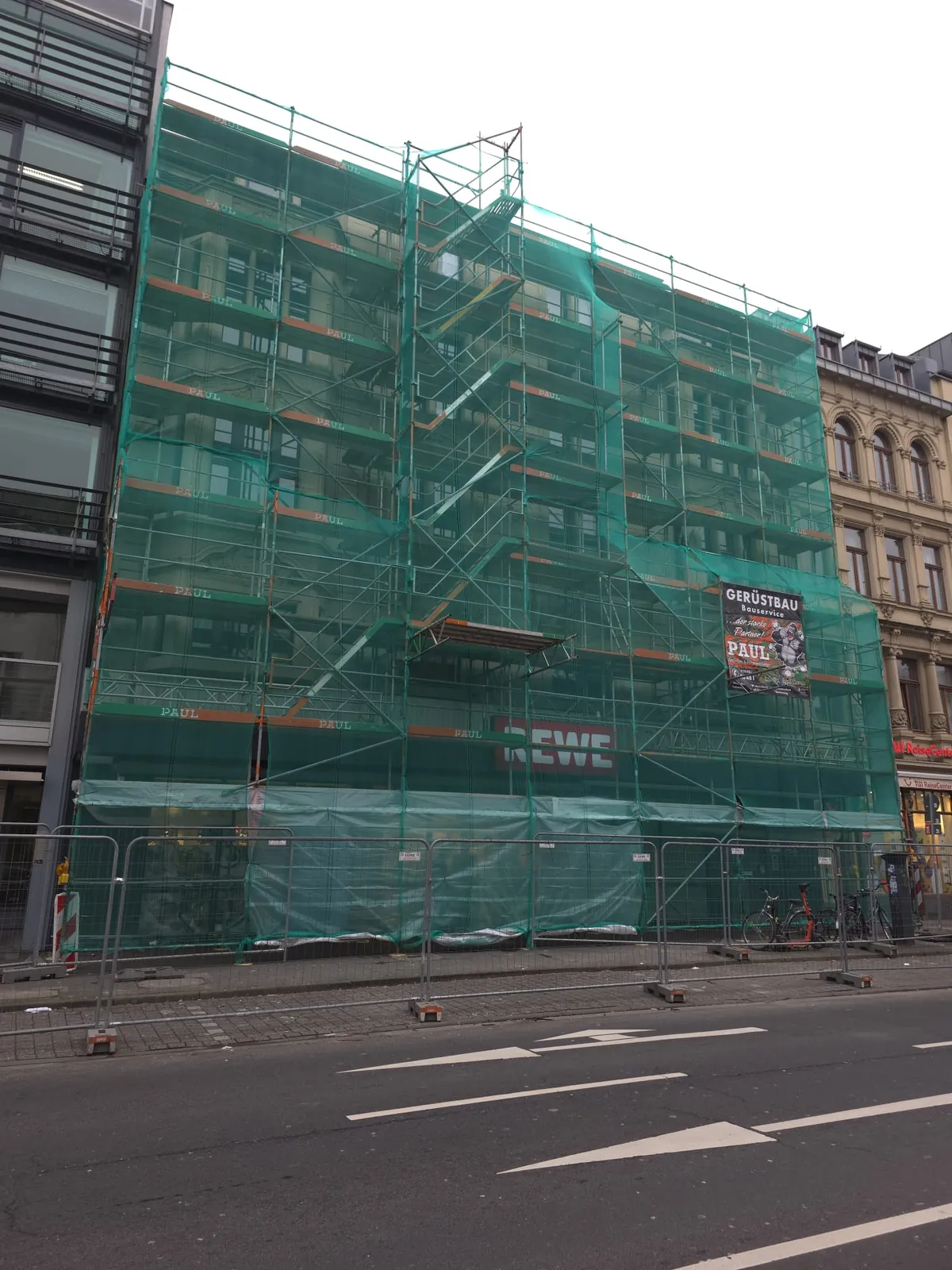 Vollflächig mit grünem Schutznetz eingerüstetes Geschäftshaus im Kölner Zentrum mit Paul-Gerüstbau-Banner