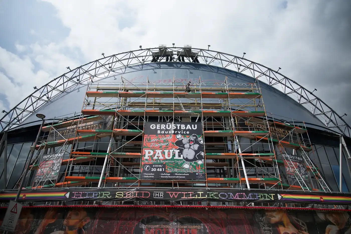 Gerüst an der gekrümmten Kuppel des Musical Dome in Köln mit Banner von Paul Gerüstbau