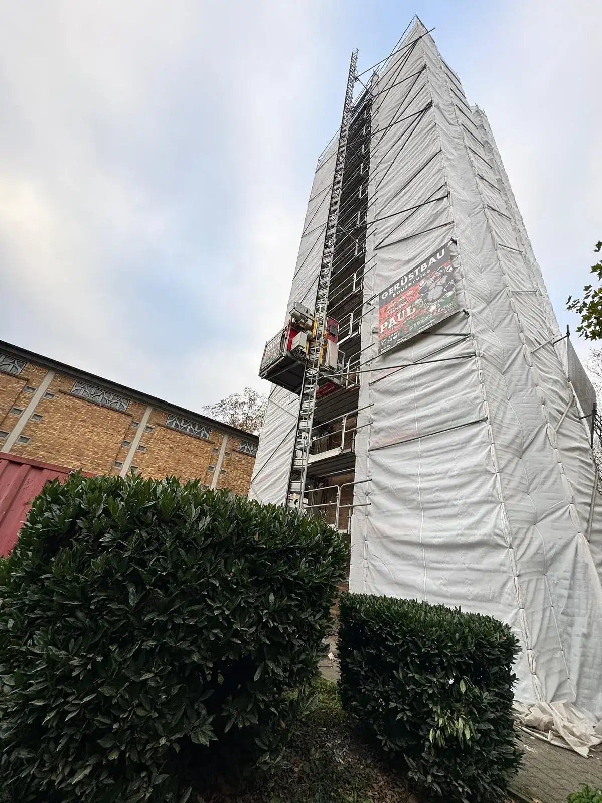 Vollflächig eingehauster Kirchturm von St. Wendelinus in Hürth mit Gerüst unter der Plane